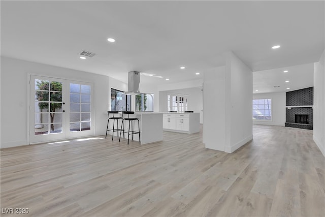 unfurnished living room with visible vents, baseboards, light wood-style flooring, a brick fireplace, and recessed lighting