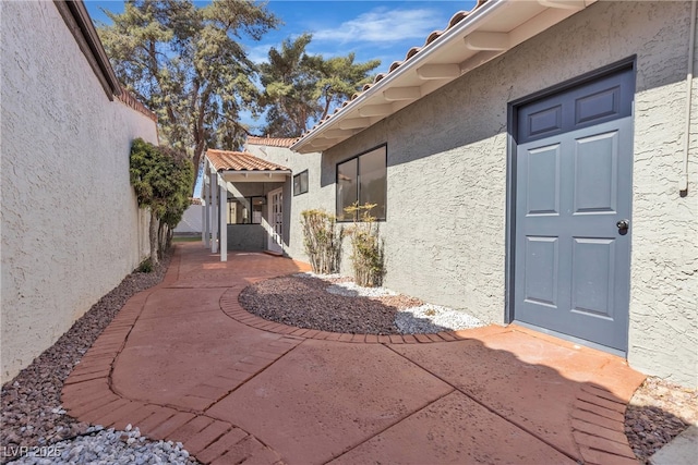 view of exterior entry featuring a tiled roof, a patio area, fence, and stucco siding