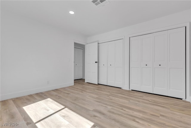 unfurnished bedroom featuring two closets, recessed lighting, visible vents, light wood-style floors, and baseboards