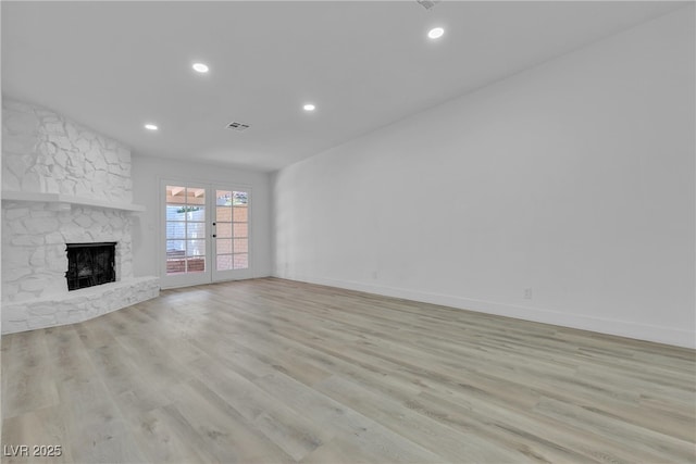 unfurnished living room featuring french doors, a fireplace, light wood-style flooring, and baseboards