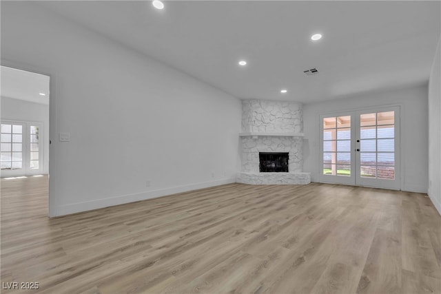 unfurnished living room with a stone fireplace, french doors, visible vents, and a healthy amount of sunlight