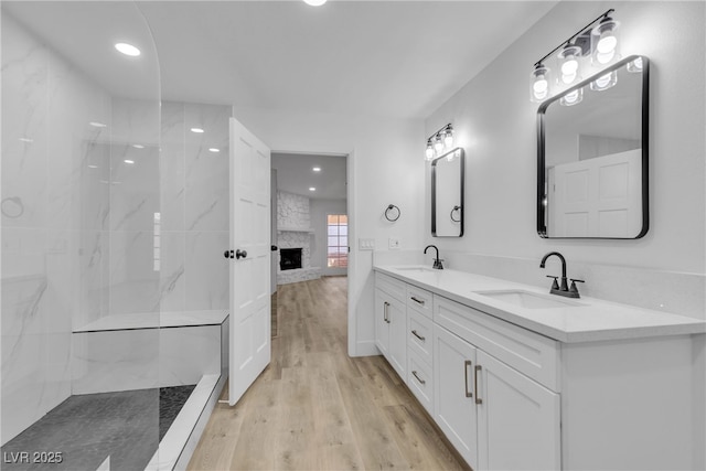 full bath featuring a large fireplace, a sink, a marble finish shower, and wood finished floors