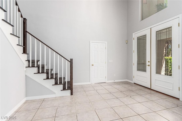 foyer featuring light tile patterned floors, baseboards, stairs, a high ceiling, and french doors