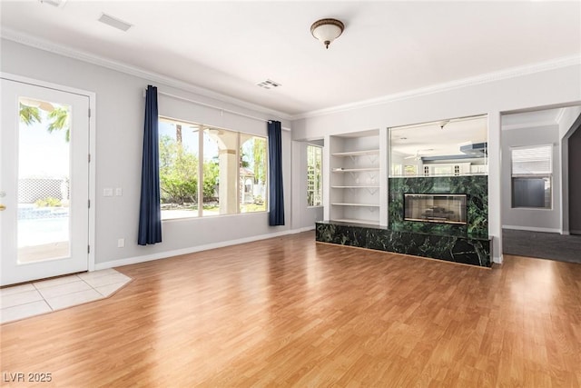 unfurnished living room featuring built in shelves, wood finished floors, visible vents, a high end fireplace, and ornamental molding