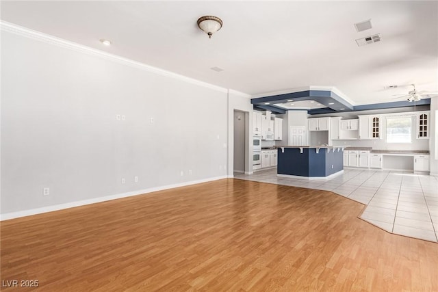 unfurnished living room with visible vents, baseboards, ceiling fan, light wood-style flooring, and ornamental molding