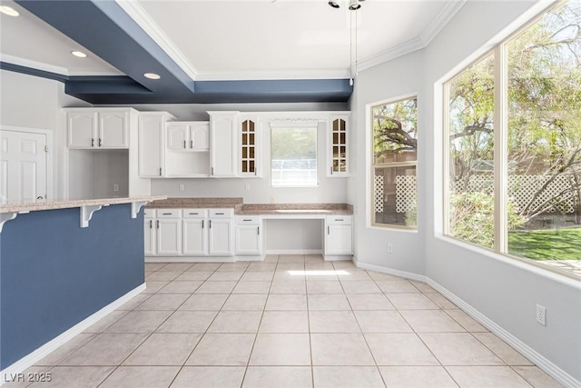 kitchen featuring ornamental molding, glass insert cabinets, built in desk, and light tile patterned floors