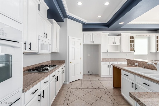 kitchen featuring white appliances, a sink, white cabinets, ornamental molding, and a tray ceiling