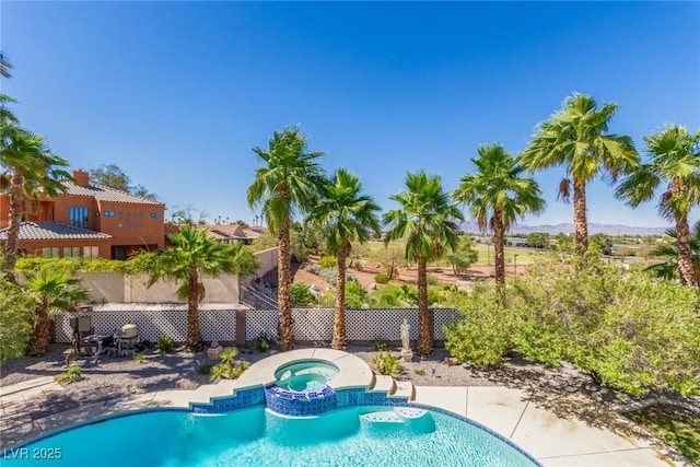 view of pool with fence and a pool with connected hot tub