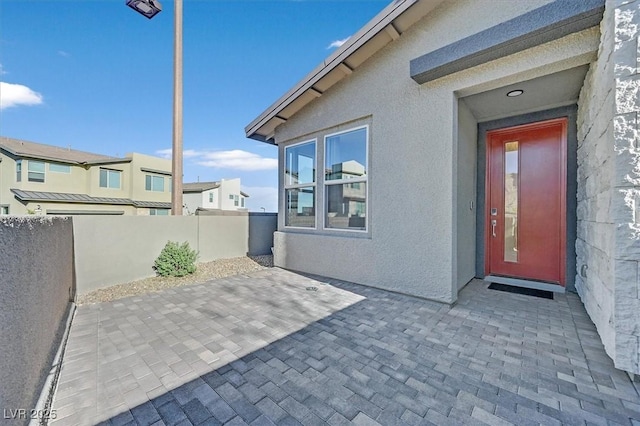 view of exterior entry with a patio area, fence, and stucco siding