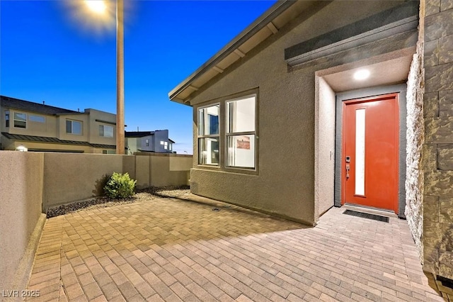 entrance to property featuring a patio area, fence, and stucco siding