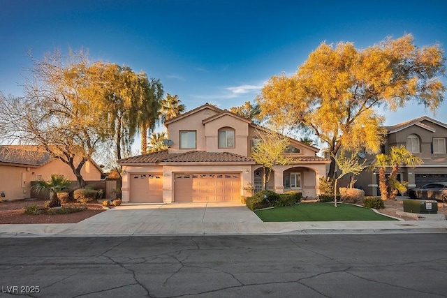 mediterranean / spanish house with a garage, concrete driveway, a tiled roof, and stucco siding