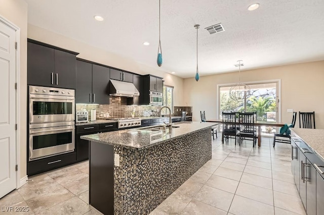 kitchen featuring visible vents, a sink, stainless steel appliances, under cabinet range hood, and backsplash