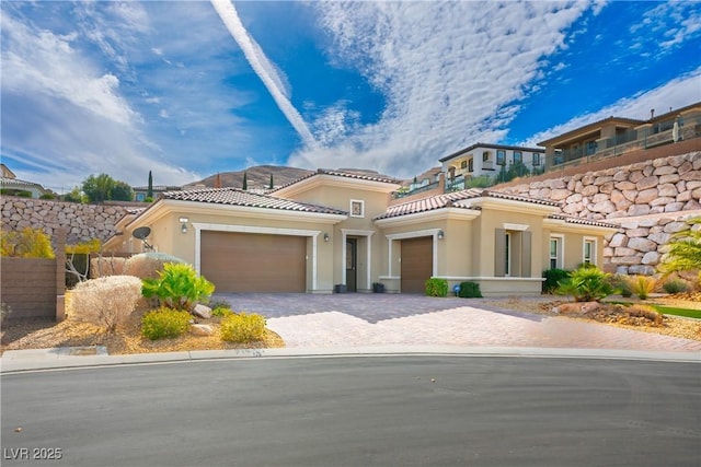 mediterranean / spanish-style house featuring a garage, decorative driveway, a tile roof, and stucco siding