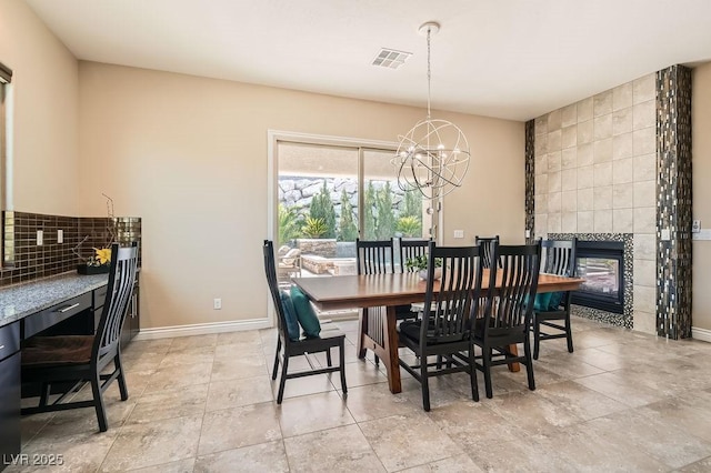 dining area with an inviting chandelier, baseboards, visible vents, and a tile fireplace