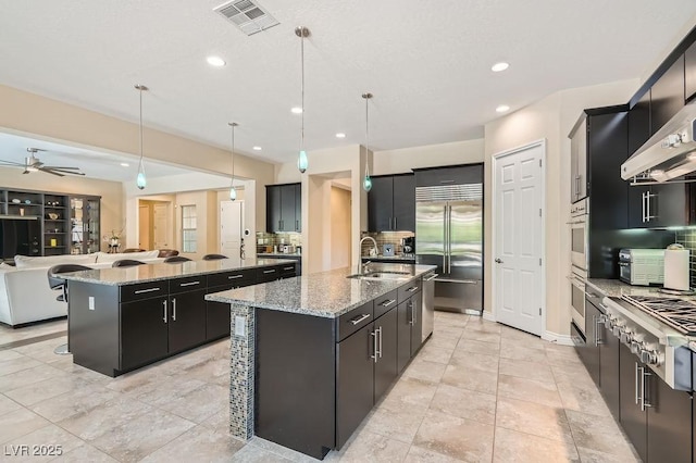 kitchen with a sink, visible vents, open floor plan, appliances with stainless steel finishes, and a center island with sink