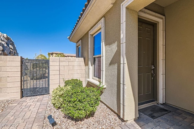 property entrance with a gate, fence, and stucco siding