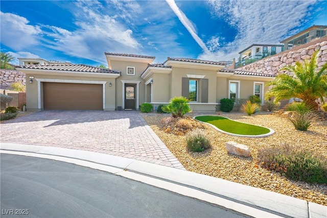 mediterranean / spanish house with an attached garage, a tile roof, decorative driveway, and stucco siding