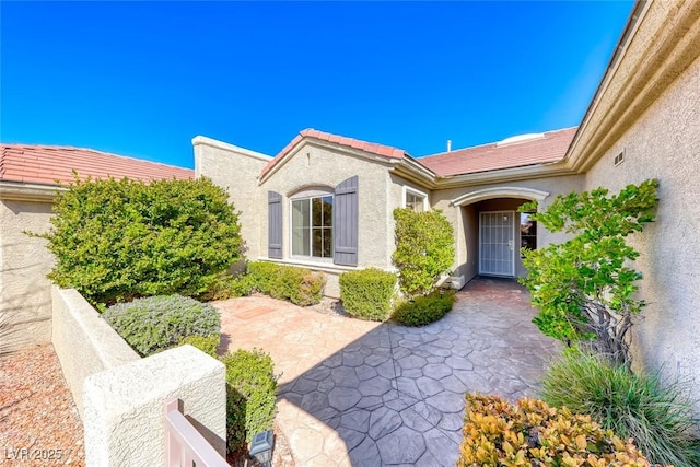 property entrance with a patio area, a tile roof, and stucco siding