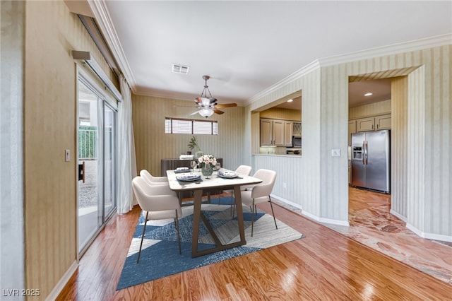 dining space with wallpapered walls, visible vents, baseboards, light wood-style flooring, and crown molding