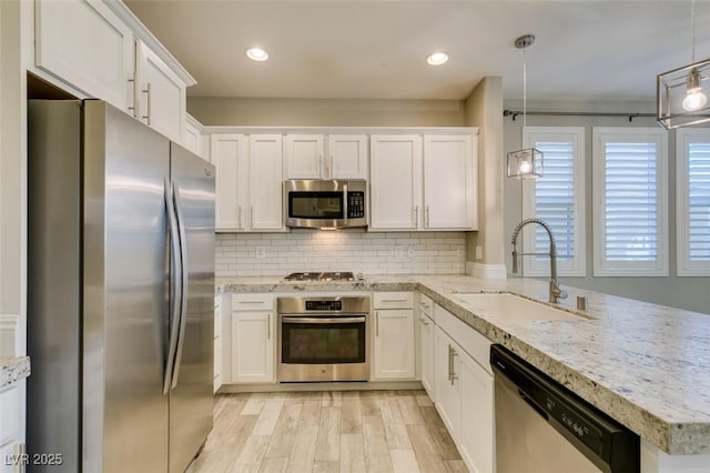 kitchen with stainless steel appliances, a peninsula, a sink, white cabinetry, and backsplash