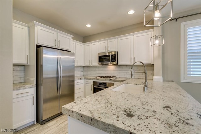 kitchen with decorative backsplash, appliances with stainless steel finishes, white cabinets, a sink, and light stone countertops