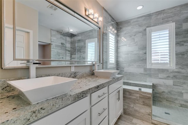 full bath featuring double vanity, visible vents, a walk in shower, and a sink