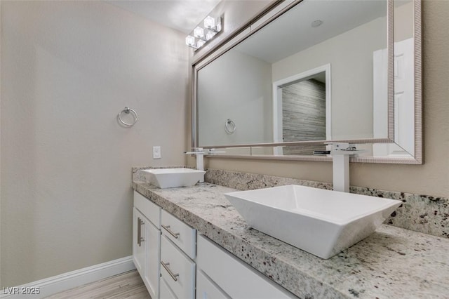 bathroom featuring double vanity, baseboards, a sink, and wood finished floors