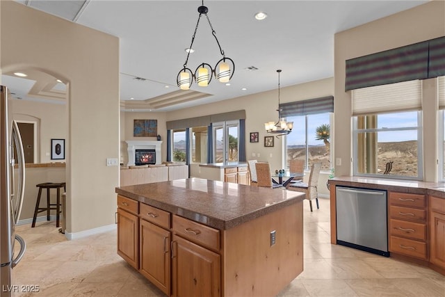 kitchen featuring a center island, stainless steel appliances, a lit fireplace, a raised ceiling, and a chandelier