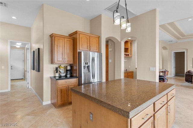 kitchen with baseboards, a kitchen island, stainless steel fridge with ice dispenser, arched walkways, and tile counters