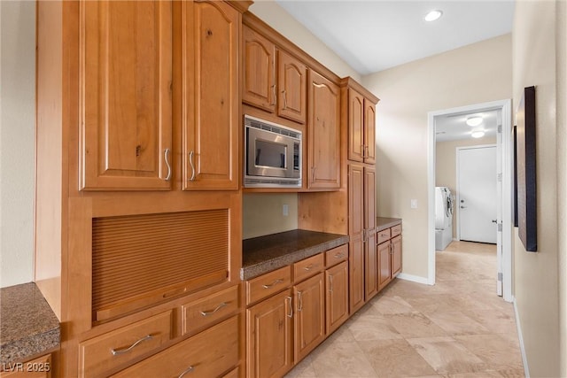 kitchen featuring brown cabinetry, dark countertops, baseboards, stainless steel microwave, and independent washer and dryer