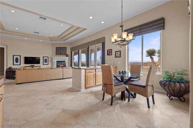 dining room with visible vents, a notable chandelier, a tray ceiling, a glass covered fireplace, and recessed lighting