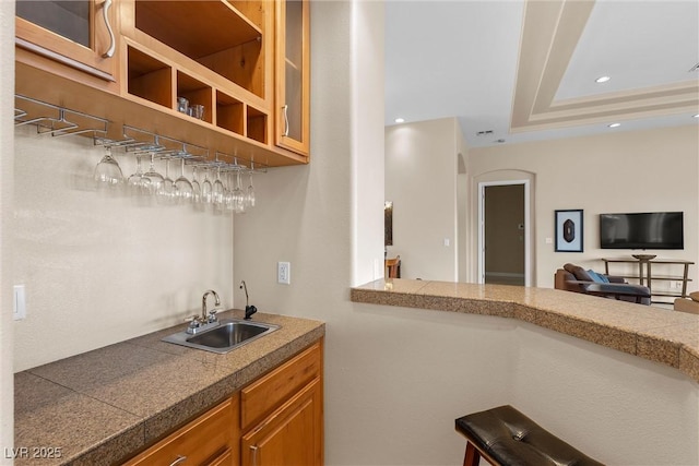 kitchen featuring tile counters, recessed lighting, glass insert cabinets, and a sink