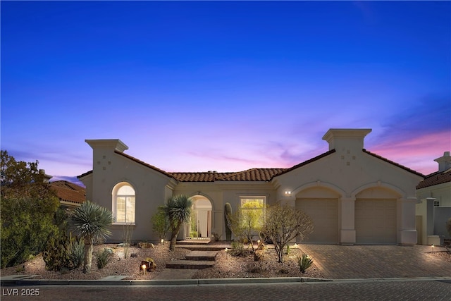 mediterranean / spanish-style home featuring stucco siding, decorative driveway, an attached garage, and a tiled roof