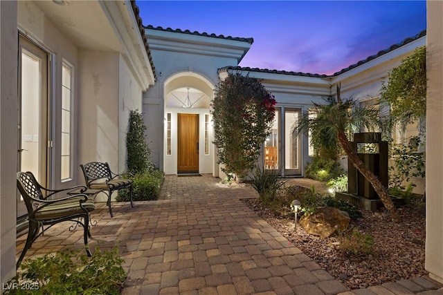 exterior entry at dusk featuring stucco siding and a tile roof