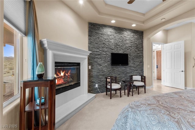 bedroom with a glass covered fireplace, recessed lighting, arched walkways, carpet, and a raised ceiling