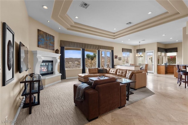 living area with visible vents, a raised ceiling, baseboards, and a glass covered fireplace