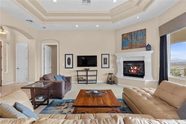 living room with a tray ceiling, visible vents, and a glass covered fireplace