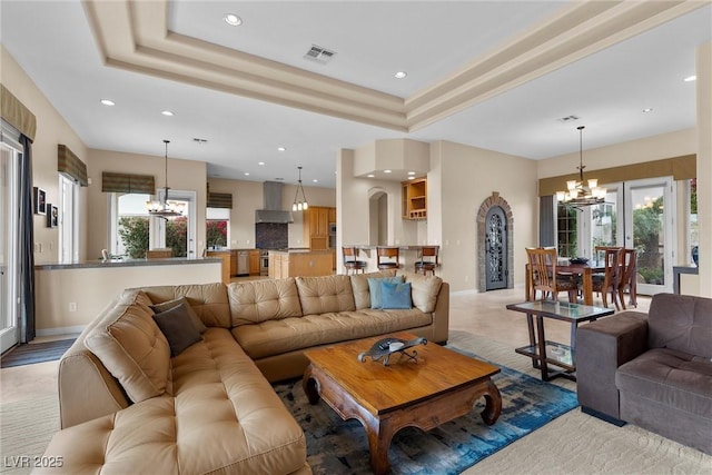 living room featuring an inviting chandelier, a healthy amount of sunlight, visible vents, and a tray ceiling