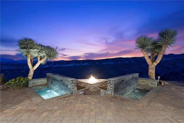 pool at dusk with a mountain view, a fire pit, and exterior kitchen