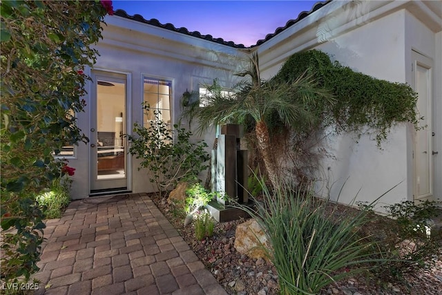 exterior entry at dusk with stucco siding and a tiled roof