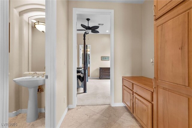 hall featuring visible vents, light colored carpet, baseboards, and a sink