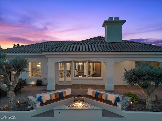 back of house featuring an outdoor living space with a fire pit, a tile roof, french doors, and stucco siding