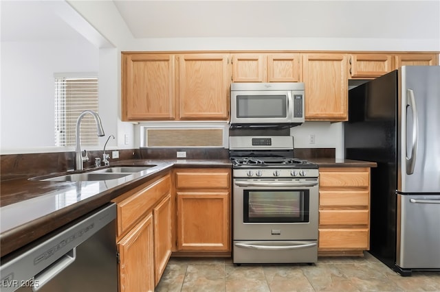 kitchen featuring dark countertops, appliances with stainless steel finishes, a sink, and light brown cabinetry