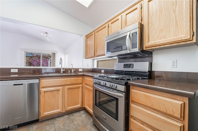 kitchen with light brown cabinets, a sink, vaulted ceiling, appliances with stainless steel finishes, and dark countertops