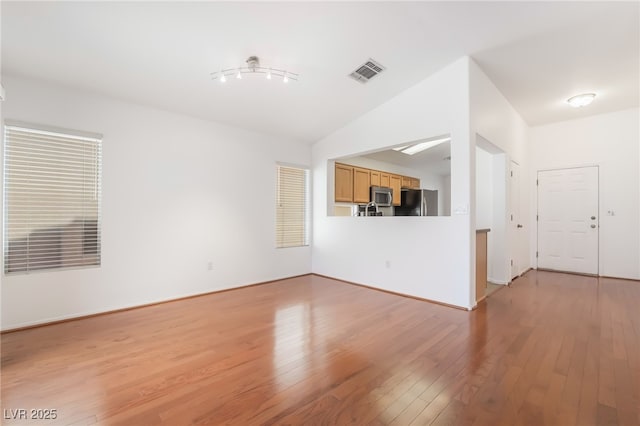 unfurnished living room with light wood-type flooring, visible vents, and lofted ceiling