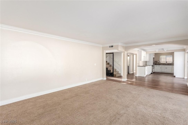 unfurnished living room with arched walkways, baseboards, ornamental molding, stairway, and dark carpet