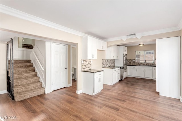 kitchen featuring dark countertops, visible vents, backsplash, light wood-style floors, and a sink