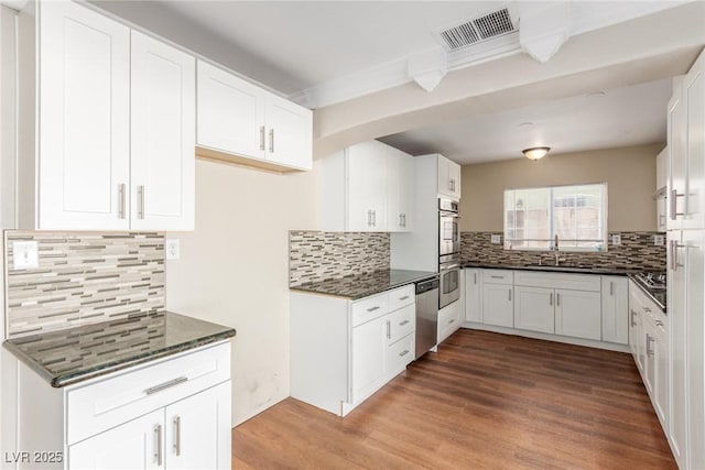 kitchen featuring stainless steel appliances, wood finished floors, a sink, visible vents, and backsplash