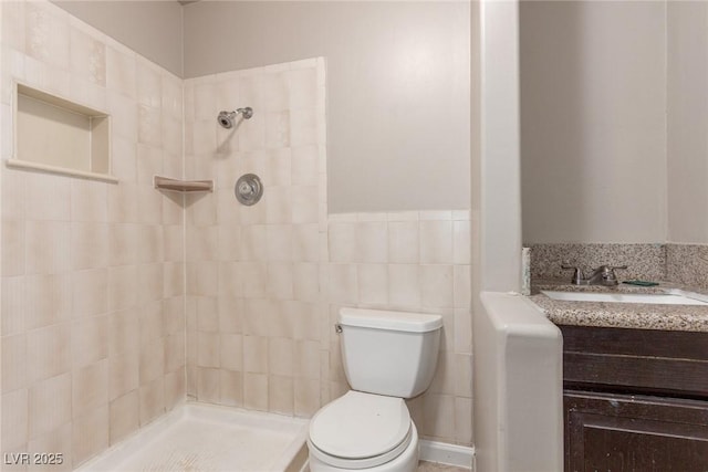 bathroom with wainscoting, toilet, a sink, a tile shower, and tile walls