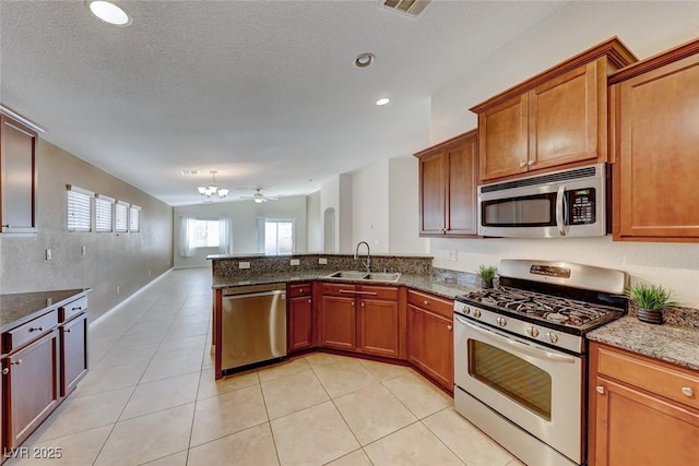 kitchen featuring light tile patterned floors, stainless steel appliances, a sink, dark stone countertops, and a peninsula